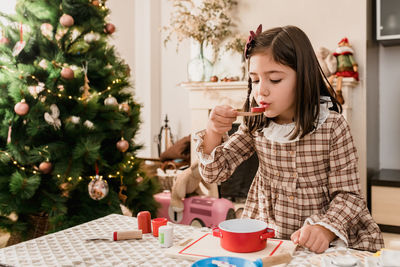 Attentive child in checkered dress playing with toys during cooking process at table in light room