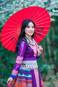 Portrait of smiling young woman with red umbrella standing outdoors