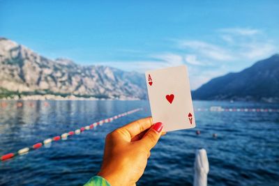 Person holding heart shape by sea against mountain