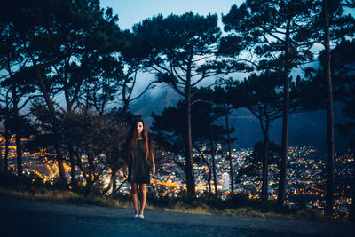 Young woman standing by trees against sky at night