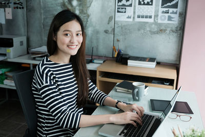 Portrait of smiling young woman using laptop while sitting at office desk