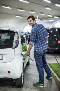 Full length portrait of young man charging electric car at gas station