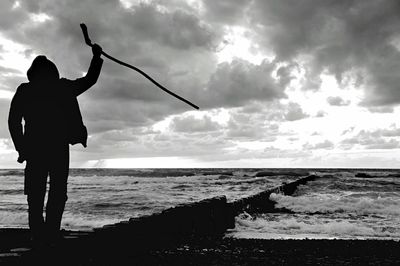 Silhouette man fishing on beach against sky