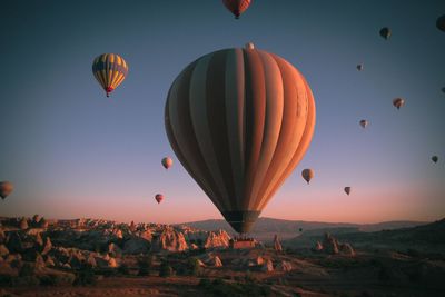 Hot air balloons flying over land against sky during sunset