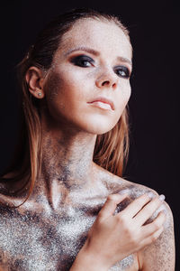 Shirtless young woman with silver glitter on her body against black background
