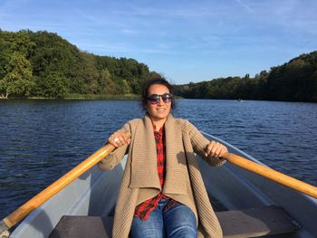 Woman oaring boat in river against sky