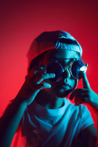 Cyberpunk boy in a white t-shirt and cap sunglasses stands against the wall and thinks