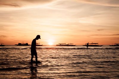 Silhouette man wading in sea against sky during sunset