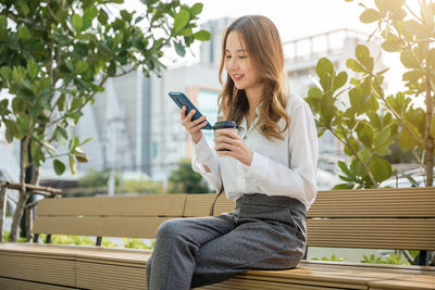 Young woman using mobile phone while sitting on bench