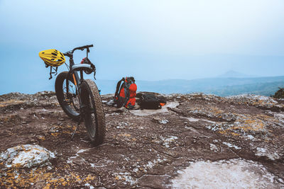 Bicycle by backpack on mountain against sky