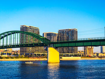 Modern buildings by river against clear blue sky