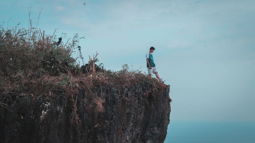 Young man walking on cliff against sky