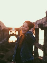 Portrait of cheerful woman standing at beach during sunset