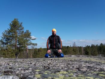 Surface level view of man kneeling on road against blue sky