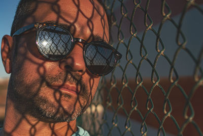 Close-up portrait of man wearing chainlink fence