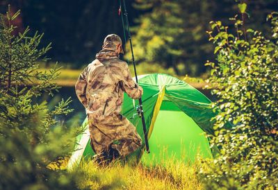 Rear view of man holding fishing rod standing by tent