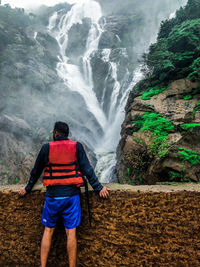 Rear view of man standing against waterfall in forest