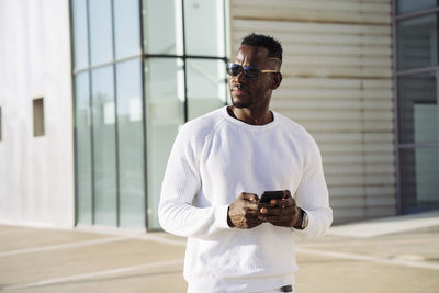 African man in sunglasses with smart phone against building