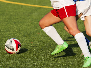 Low section of people playing soccer ball on grass