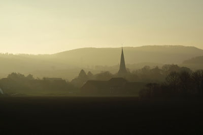 Silhouette of temple and building against sky