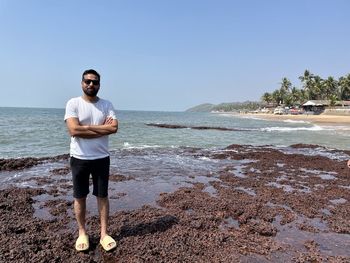 Portrait of young man standing at beach against clear sky