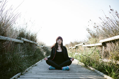 Woman meditating on boardwalk amidst grass