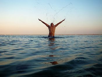 Shirtless man splashing water in sea during sunset