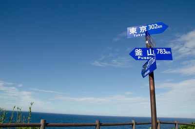 Low angle view of information signs by sea against blue sky