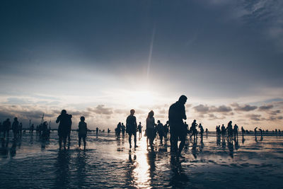 Silhouette people on beach against sky during sunset