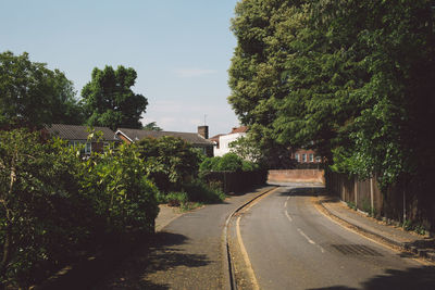 Empty road amidst trees and buildings against sky