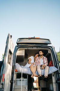 Low angle side view of traveling couple sitting on bed in camper and embracing during summer trip