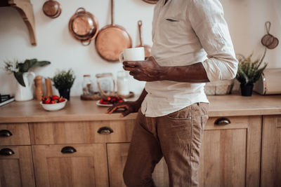 Midsection of man standing with coffee at home