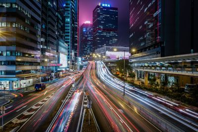 Light trails over street amidst illuminated buildings at night