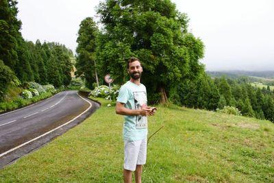 Portrait of young man standing on grass field against sky