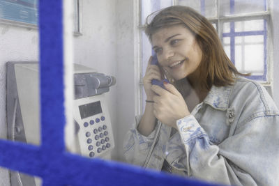 Cheerful woman using phone in telephone booth outdoors