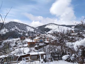 Snow covered houses by mountain against sky