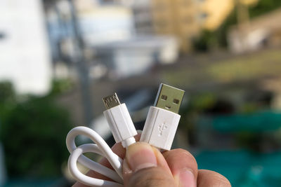 Close-up of hand holding usb cable against buildings