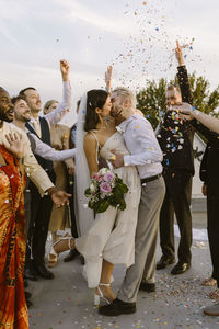 Romantic couple kissing each other while guests celebrating with confetti at wedding celebration on rooftop