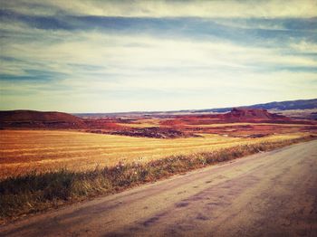 Road passing through field against cloudy sky