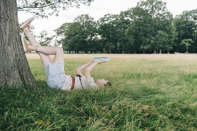 Woman reading book while relaxing on grass at park