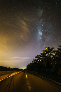 Road amidst trees against sky at night