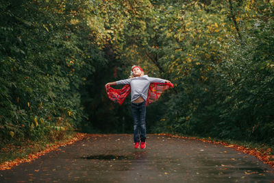 Cute girl jumping on road in forest during autumn