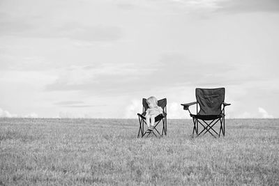 Girl sitting on chair in field against sky