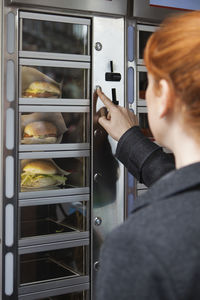 Rear view of woman buying burger in vending machine