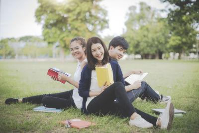 Portrait of friends studying while sitting on land in park