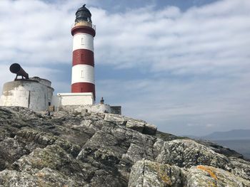 Lighthouse by buildings against sky