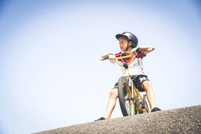 Low angle view of boy sitting on bicycle at sports ramp against clear sky