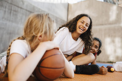 Portrait of girl laughing while sitting with female friends at basketball court