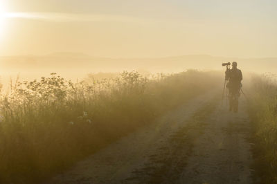 Rear view of photographer walking along dirt road