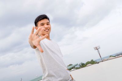 Portrait of smiling young man showing stop gesture against sky